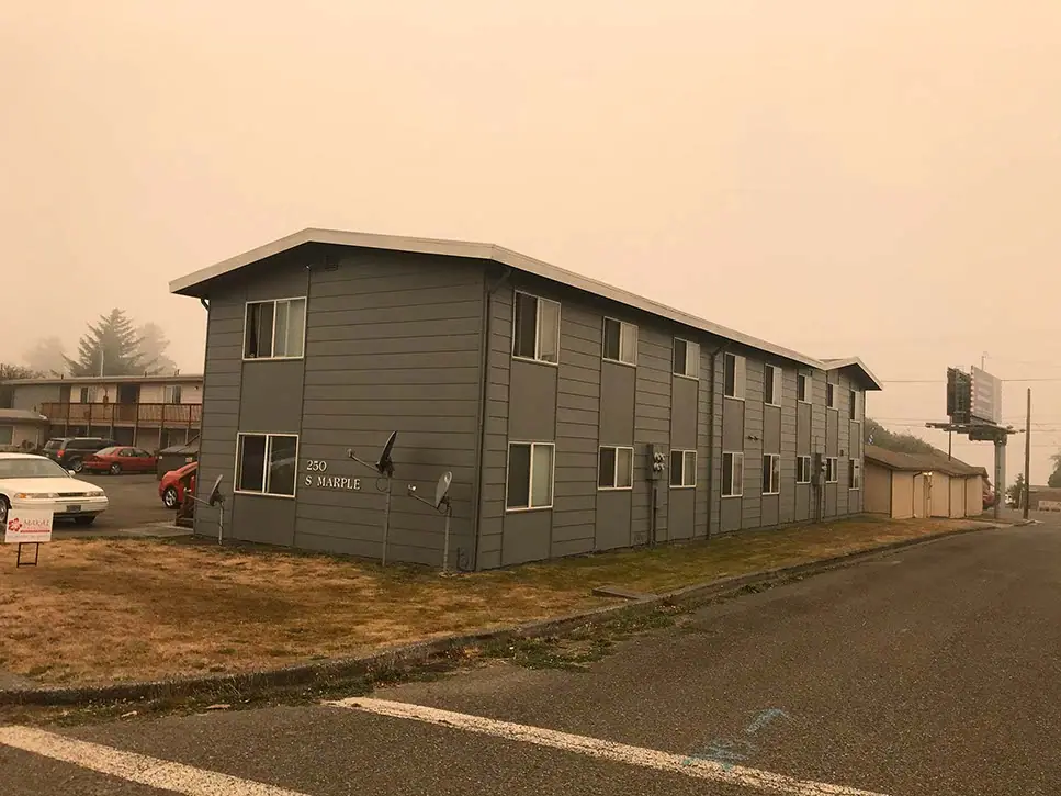 A two-story apartment building in gray with white trim, under an orange sky