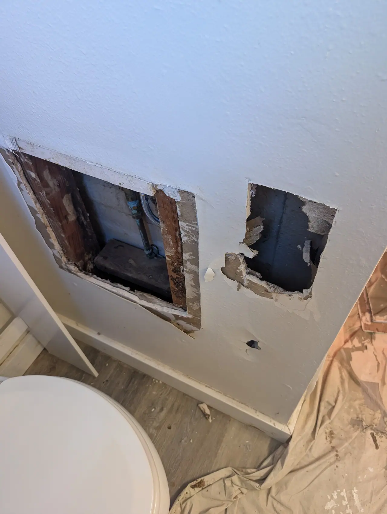 A bathroom wall opened beside the toilet for a repair