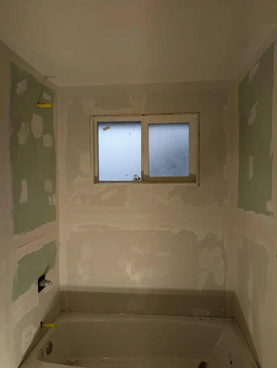 A tub alcove with green wallboard, patched and not yet primed