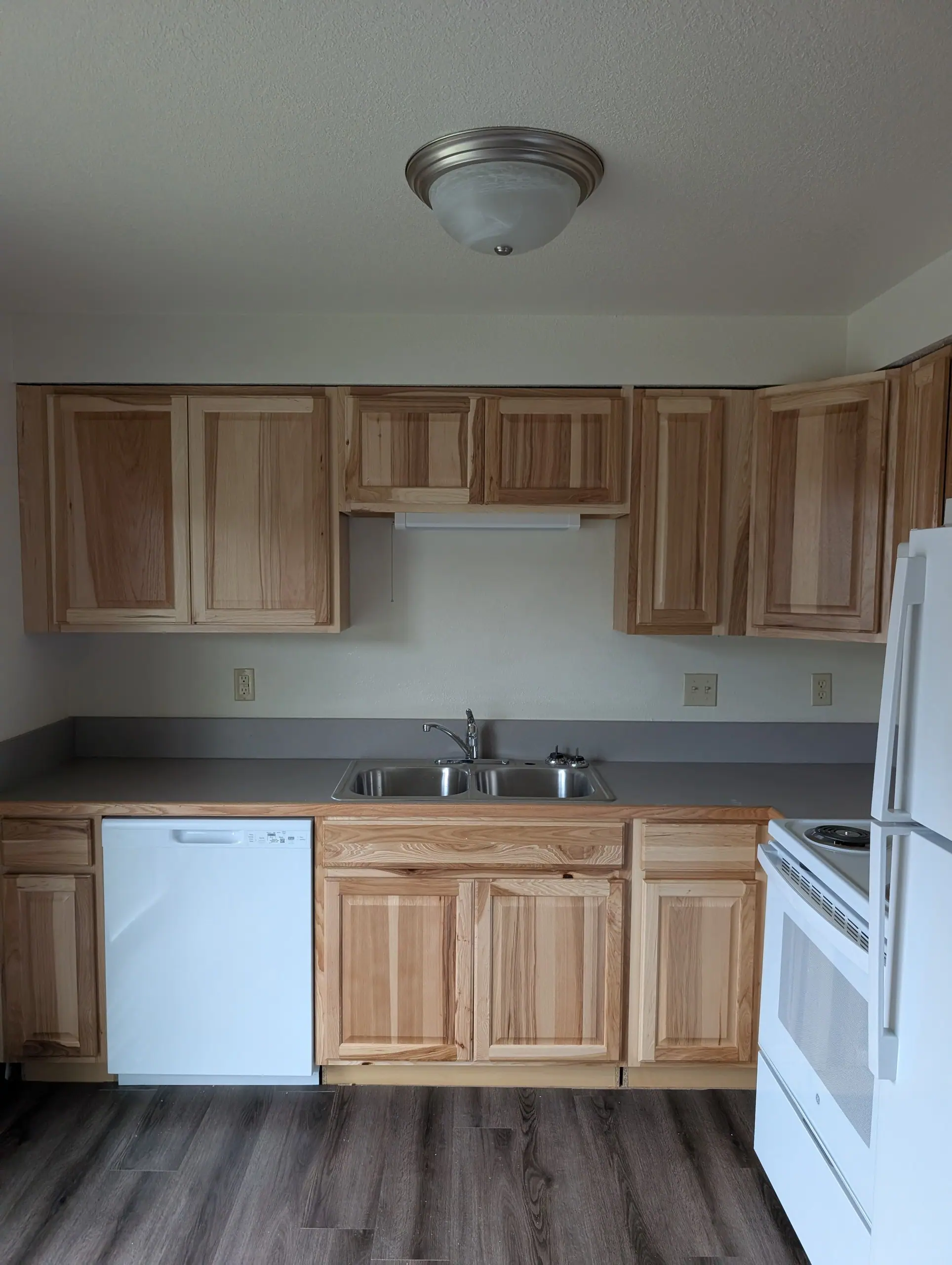 An apartment kitchen after a turnover: hickory cabinets, white appliances, a gray plank floor