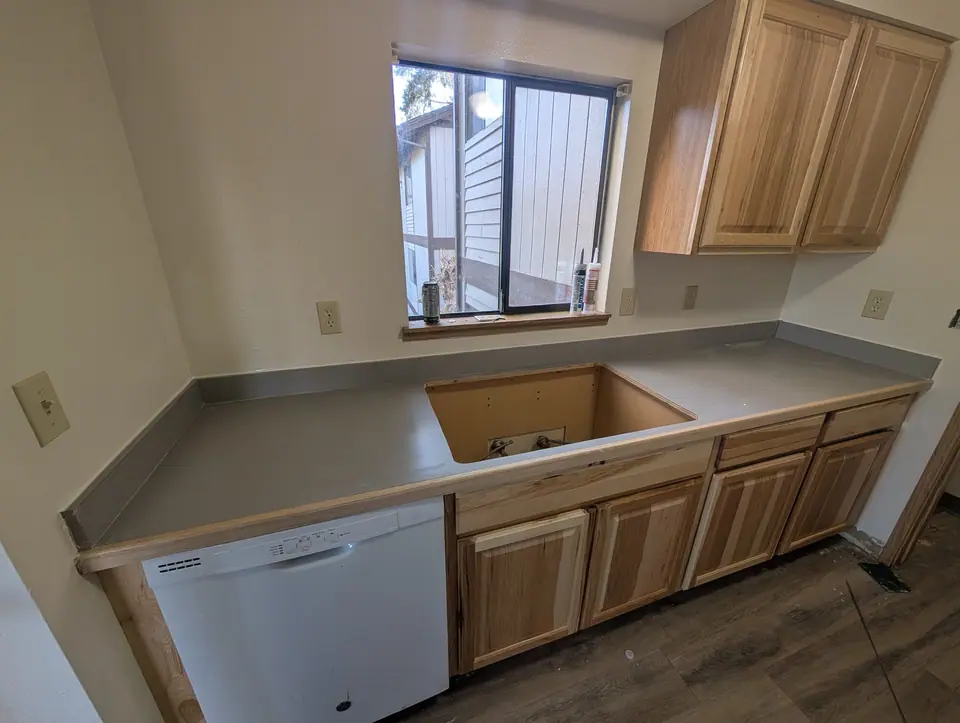 A kitchen with new wood cabinets and countertop, the sink not yet set
