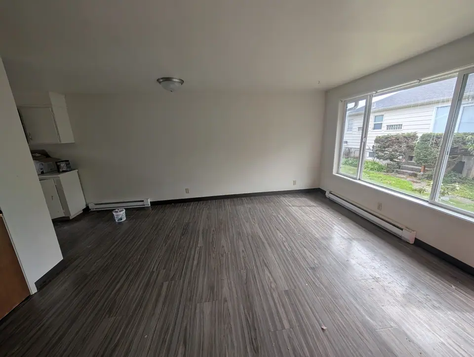 An empty living room with a big window, white walls and a gray plank floor