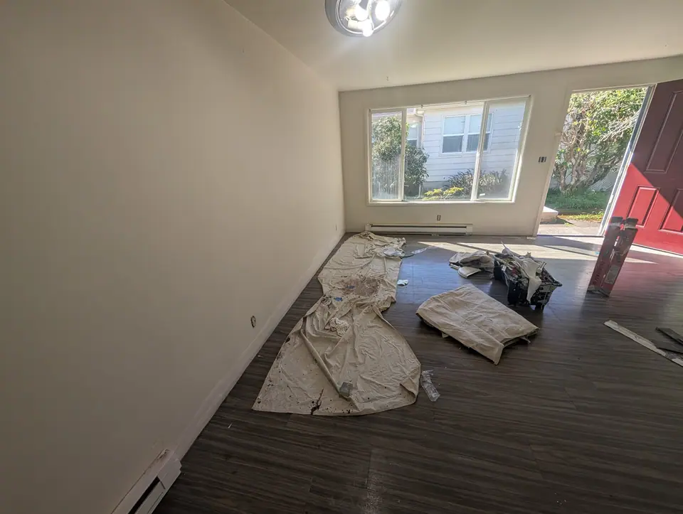 An apartment living room mid-repaint, drop cloths down and the red front door open