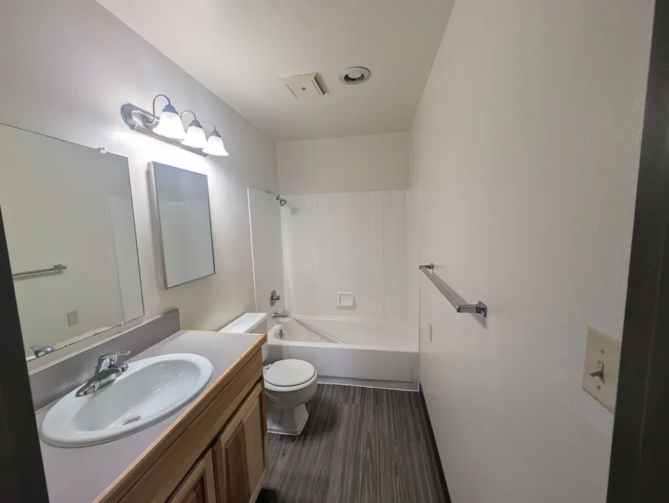 An apartment bathroom after a turnover: a wood vanity, the tub and fresh white walls