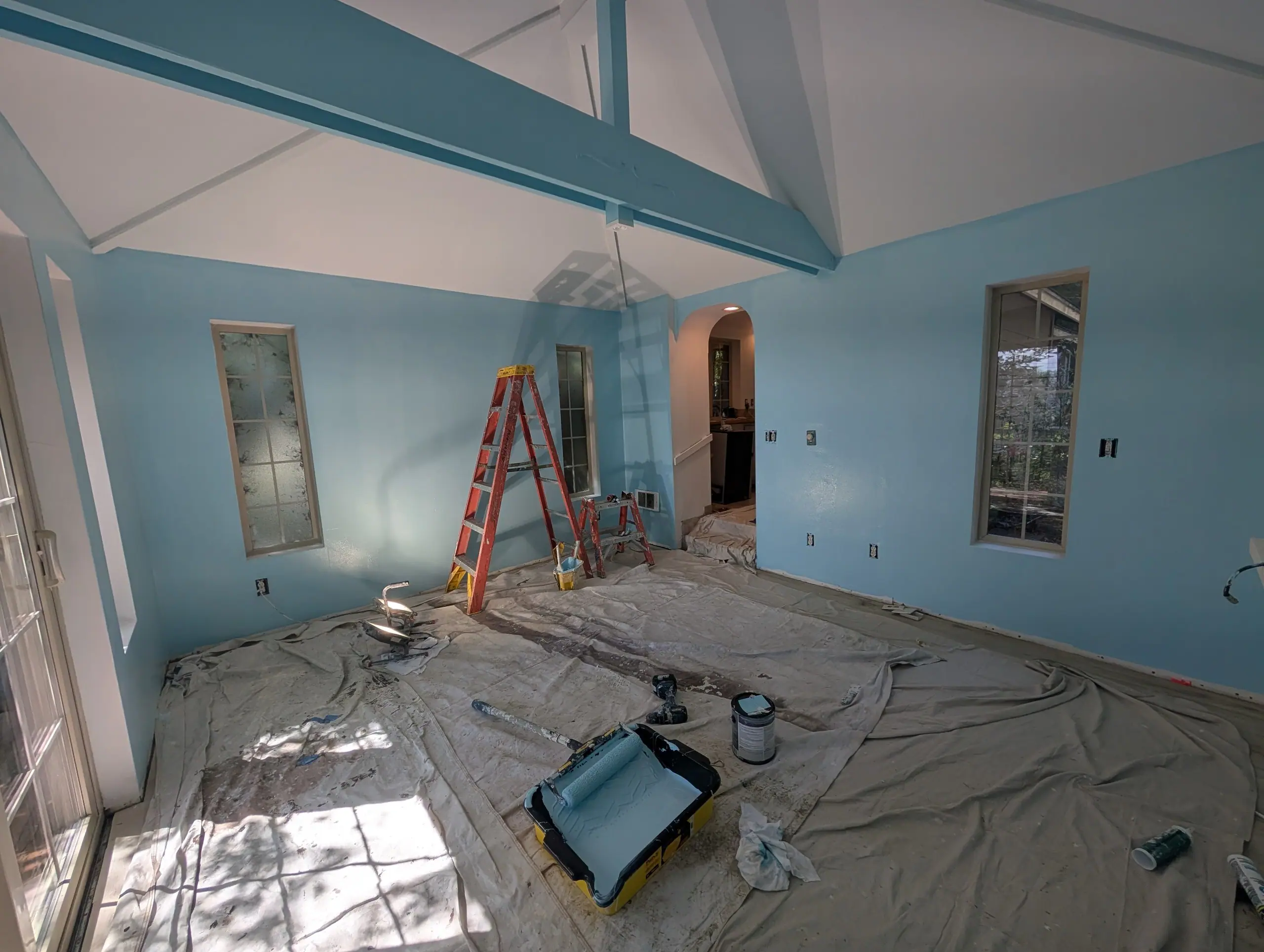 A vaulted living room painted blue, a ladder and drop cloths still out