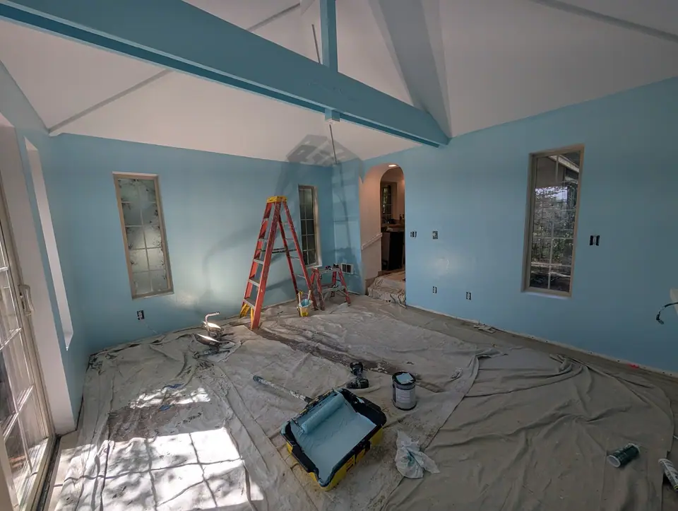 A vaulted living room painted blue, a ladder and drop cloths still out