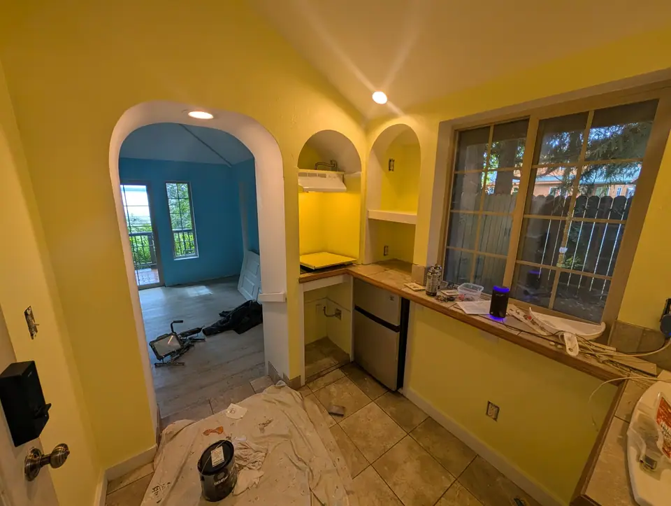 A cottage kitchenette painted yellow, with arched niches and an arch into a blue room