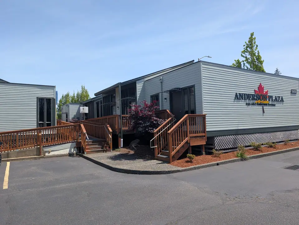 A commercial building with light gray siding, dark trim and wood stairs to the entry