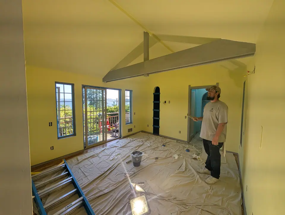 A Makai painter in a yellow room with gray beams, drop cloths on the floor