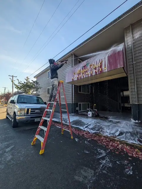 A Makai crew member on a ladder pressure washing an apartment entry awning